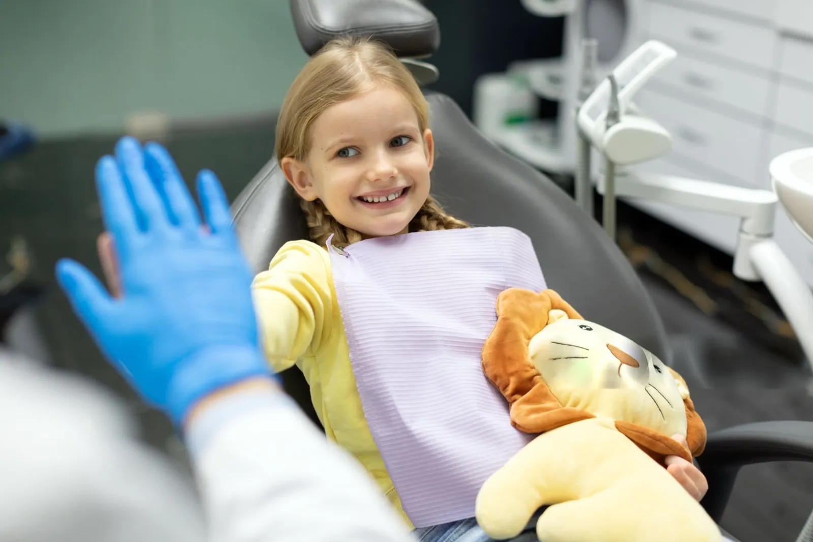 Smiling young girl in the dental chair giving a high five