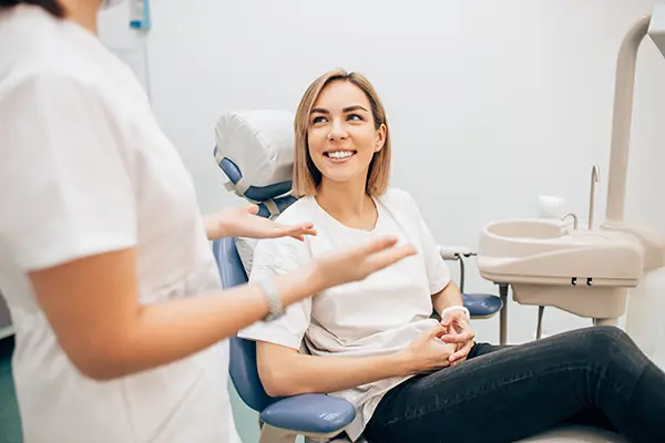 Smiling patient sitting a dental chair while her dental assistant speaks with her.